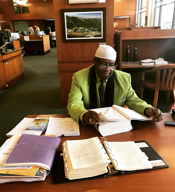 Photograph of a man sitting at a table reaching a law book.